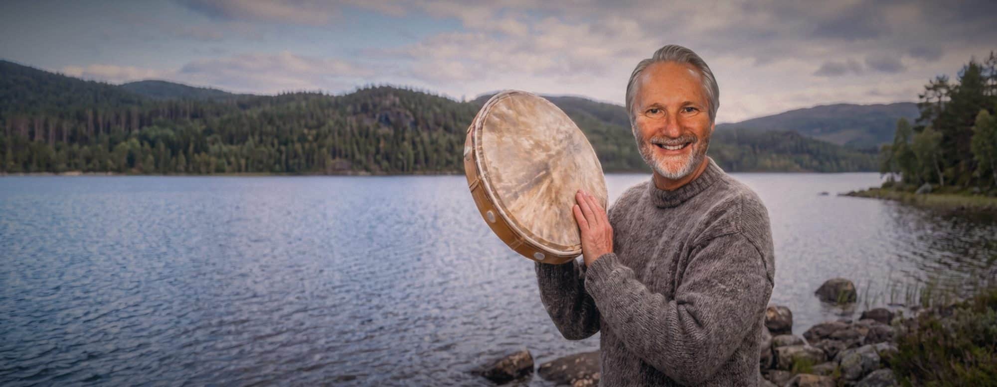 Pål-Esben Wanvig med tromme ved et skogsvann i kveldslys.
